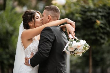 Kahverengi takım elbiseli damat ve şehir ortamında beyaz elbiseli gelin.