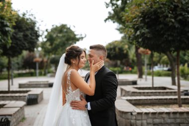 Kahverengi takım elbiseli damat ve şehir ortamında beyaz elbiseli gelin.