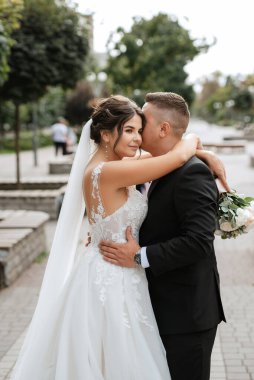 Kahverengi takım elbiseli damat ve şehir ortamında beyaz elbiseli gelin.