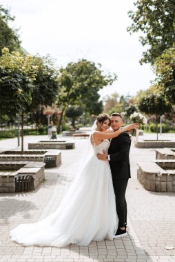 Kahverengi takım elbiseli damat ve şehir ortamında beyaz elbiseli gelin.