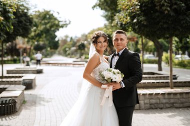 Kahverengi takım elbiseli damat ve şehir ortamında beyaz elbiseli gelin.