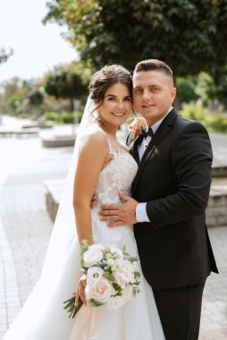 Kahverengi takım elbiseli damat ve şehir ortamında beyaz elbiseli gelin.