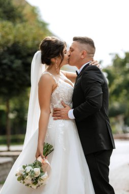 Kahverengi takım elbiseli damat ve şehir ortamında beyaz elbiseli gelin.