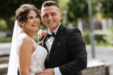 Kahverengi takım elbiseli damat ve şehir ortamında beyaz elbiseli gelin.