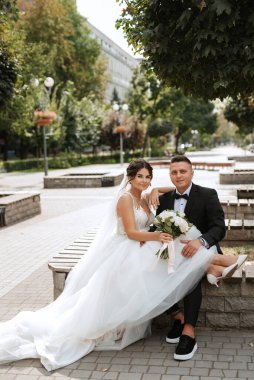 Kahverengi takım elbiseli damat ve şehir ortamında beyaz elbiseli gelin.