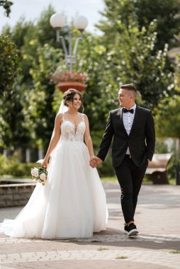 Kahverengi takım elbiseli damat ve şehir ortamında beyaz elbiseli gelin.