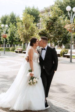 Kahverengi takım elbiseli damat ve şehir ortamında beyaz elbiseli gelin.