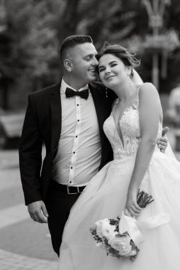 Kahverengi takım elbiseli damat ve şehir ortamında beyaz elbiseli gelin.