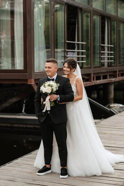 the first meeting of the bride and groom in wedding dresses on the pier near the water