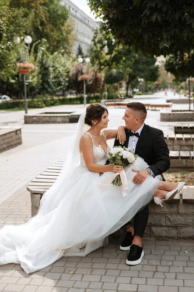 Kahverengi takım elbiseli damat ve şehir ortamında beyaz elbiseli gelin.