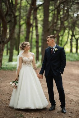 the groom and the bride are walking in the forest on a bright day