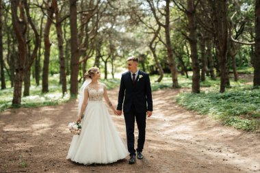 the groom and the bride are walking in the forest on a bright day