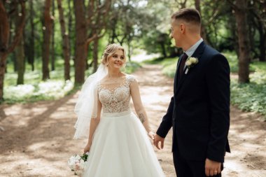 the groom and the bride are walking in the forest on a bright day