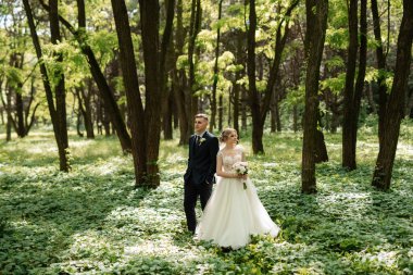 the groom and the bride are walking in the forest on a bright day