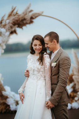 Gelin ve damadın ilk düğün dansı nehir kıyısındaki iskelede, düğün kemerinin arka planında.