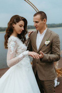 Gelin ve damadın ilk düğün dansı nehir kıyısındaki iskelede, düğün kemerinin arka planında.