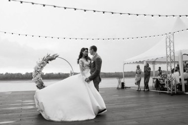 Gelin ve damadın ilk düğün dansı nehir kıyısındaki iskelede, düğün kemerinin arka planında.