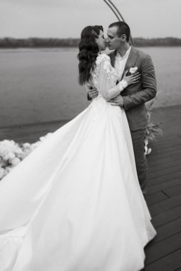 Gelin ve damadın ilk düğün dansı nehir kıyısındaki iskelede, düğün kemerinin arka planında.