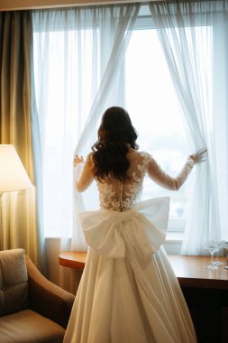 Kahverengi saçlı kız sabahları bir otel odasında gelinlik giyer.