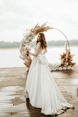 Gelin, sarı bir günbatımının arka planında nehir kıyısındaki bir iskelede