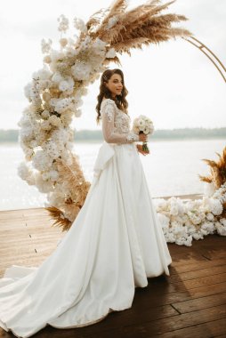 Gelin, sarı bir günbatımının arka planında nehir kıyısındaki bir iskelede