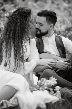 Sakallı bir damat telli bir enstrüman çalar ve yeşil saçlı bir kız baharda çayırda oturur.