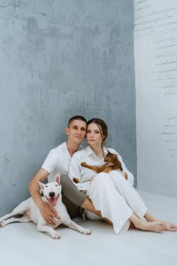 Genç bir çift, parlak bir odada kedi ve köpekle oynuyorlar.