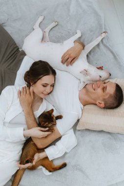 Genç bir çift, parlak bir odada kedi ve köpekle oynuyorlar.