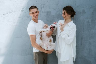 Genç bir çift, parlak bir odada köpekle oynuyorlar.