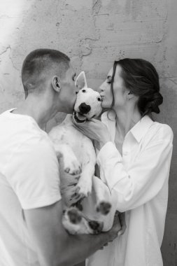 Genç bir çift, parlak bir odada köpekle oynuyorlar.