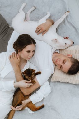 Genç bir çift, parlak bir odada kedi ve köpekle oynuyorlar.