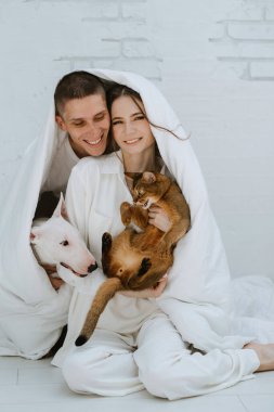 Genç bir çift, parlak bir odada kedi ve köpekle oynuyorlar.