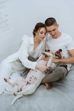 Genç bir çift, parlak bir odada köpekle oynuyorlar.