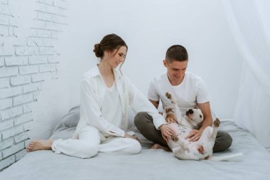 Genç bir çift, parlak bir odada köpekle oynuyorlar.