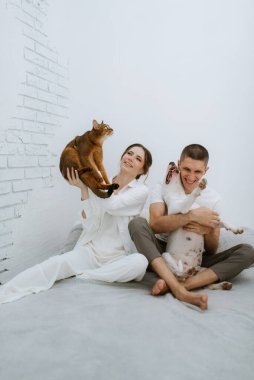 Genç bir çift, parlak bir odada kedi ve köpekle oynuyorlar.