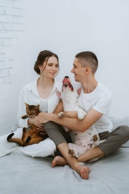 Genç bir çift, parlak bir odada kedi ve köpekle oynuyorlar.