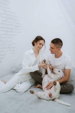 Genç bir çift, parlak bir odada köpekle oynuyorlar.