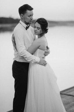 bride and groom against the backdrop of a yellow sunset on a pier near the river