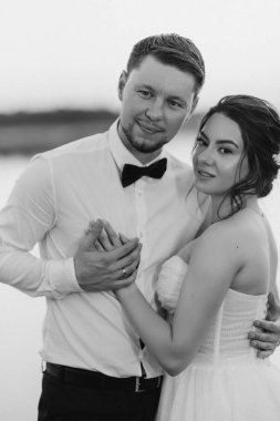 Gelin ve damat, nehrin kıyısındaki bir iskelede sarı bir günbatımının arkaplanına karşı.