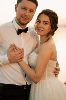 bride and groom against the backdrop of a yellow sunset on a pier near the river