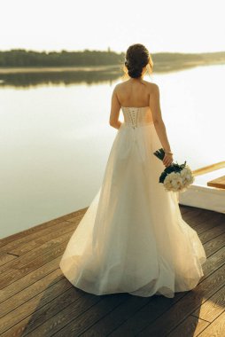 bride against the background of a yellow sunset on a pier near the river