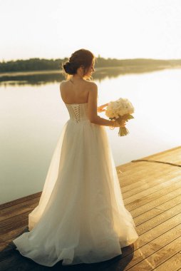 Gelin, sarı bir günbatımının arka planında nehir kıyısındaki bir iskelede