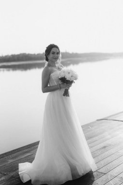 Gelin, sarı bir günbatımının arka planında nehir kıyısındaki bir iskelede