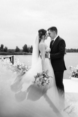 Gelin ve damat, nehrin kıyısındaki bir iskelede sarı bir günbatımının arkaplanına karşı.