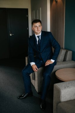 Düğün günü otelde kravatlı, mavi takım elbiseli bir damat portresi.