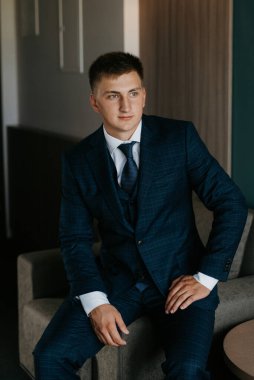 Düğün günü otelde kravatlı, mavi takım elbiseli bir damat portresi.