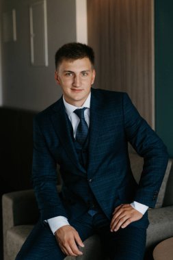 Düğün günü otelde kravatlı, mavi takım elbiseli bir damat portresi.