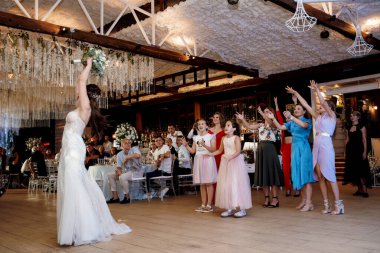 bride in a white dress throws a wedding bouquet to her unmarried girlfriends