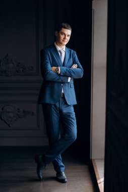 Düğün günü otelde kravatlı, mavi takım elbiseli bir damat portresi.