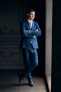 Düğün günü otelde kravatlı, mavi takım elbiseli bir damat portresi.